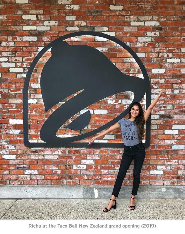 Richa at the Taco Bell New Zealand grand opening (2019) standing next to brick wall with large Taco Bell logo